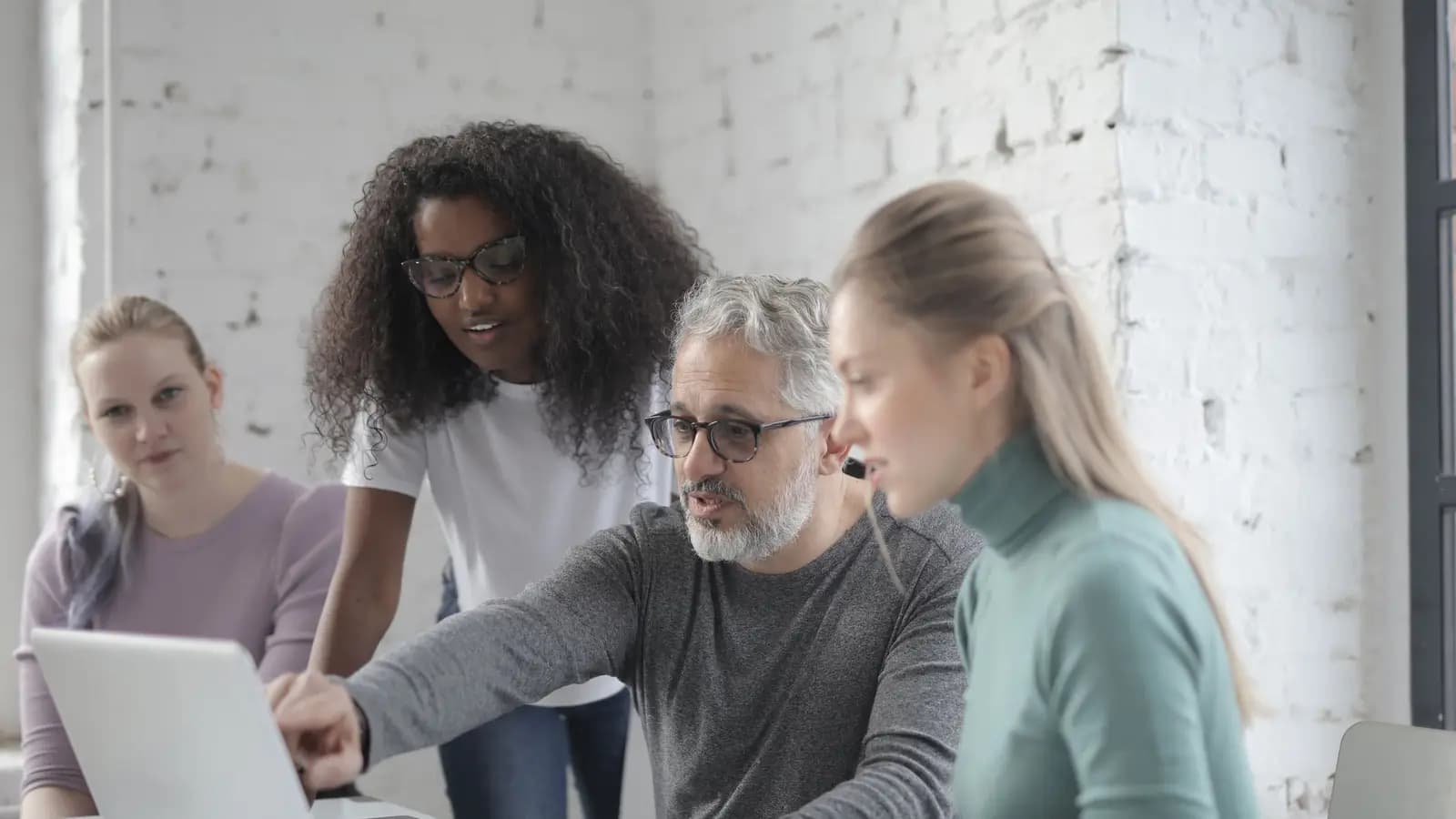 Four colleagues gathered around a laptop in a bright office